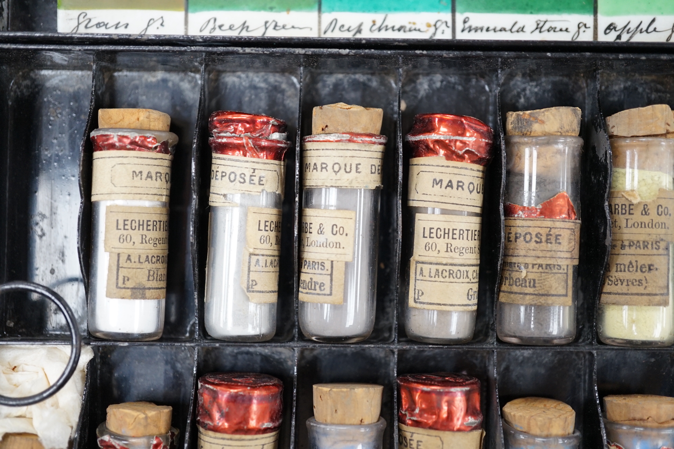 A black artist's tin box, with fitted interior, containing glass phialls of coloured shades of powdered paint and a white glass samples panel etc, box 37.5cm wide, 27cm deep